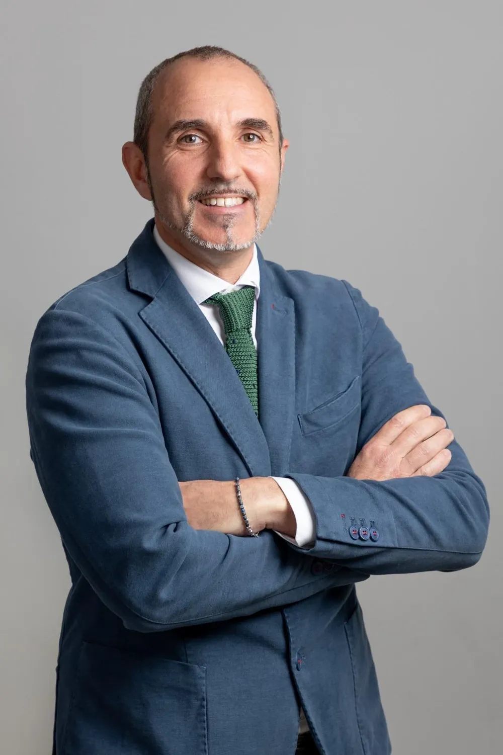 Giuseppe Zizza sorridente, in giacca blu e cravatta verde, con le braccia incrociate